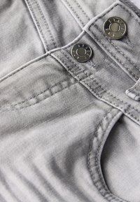Gros plan sur un tissu en denim gris avec des boutons métalliques argentés et des détails de couture, mettant en avant la texture douce et le design structuré.