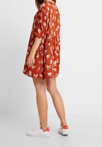 Robe rouge à motifs avec manches courtes, forme évasée, design floral et à pois. Portée avec des baskets blanches comportant des accents rouges.