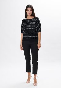Pull en maille noire avec des rayures horizontales blanches, décolleté large et manches au coude, associé à un pantalon noir ajusté et des talons argentés à lanières.