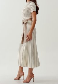 Robe crème à rayures avec des manches courtes et une taille ceinturée. Jupe fluide mi-longue, tissu doux et lignes verticales subtiles.