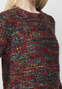 Multikleurige gebreide trui met een textuurpatroon van rode, groene, gele en paarse draden, ronde halslijn en korte mouwen.