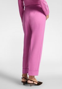 Roze op maat gemaakte broeken met een hoge taille, omslagranden en een soepele textuur, gecombineerd met donkerbruine, gestructureerde haksandalen.