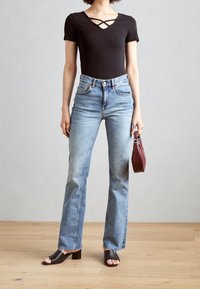 Svart bodysuit med korsande halsringning, ljusblå högmidjade utsvängda jeans och mörkbruna öppna trampor. Håller en liten vinröd väska.