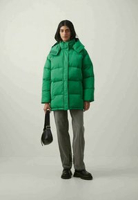 Grüne Pufferjacke mit hohem Kragen und reichlich Polsterung. Mit Reißverschluss- und Druckknopfverschluss, Seitentaschen und einer glatten Stoffoberfläche.