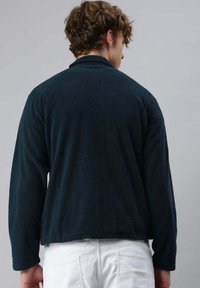 Pullover in pile di un blu navy scuro, caratterizzato da una texture morbida, maniche lunghe e un orlo corto. Nessuna chiusura visibile o elementi di design prominenti.