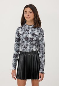 Maglietta a maniche lunghe in motivo marmorizzato bianco e nero, abbinata a una gonna plissettata in ecopelle nera. Texture liscia, silhouette aderente.