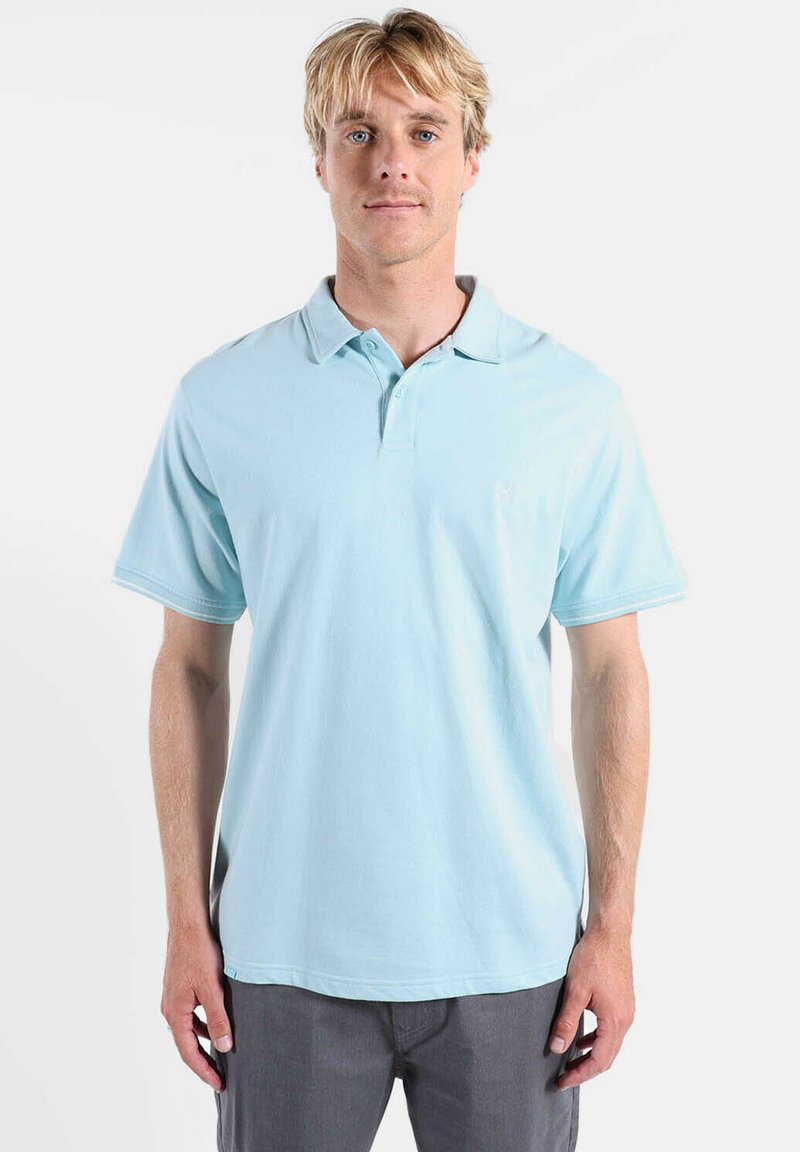 Polo bleu clair en coton avec un col classique, des manches courtes, et un logo discret sur la poitrine. Texture lisse et coupe décontractée.