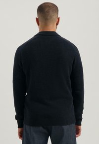 Marineblauer Strickpullover mit strukturiertem Finish, der über einen Kragen und gerippte Bündchen verfügt. Das Design ist an der Taille und Hüfte tailliert.