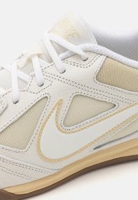 Valkoiset ja beige lenkkarit, joissa on nahka- ja verkkomateriaaleja, teksturoidut yksityiskohdat ja voimakas swoosh-korostus. Kevyt kumipohja.