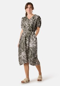 Vestito verde con scollo a V e maniche corte a sbuffo, caratterizzato da un motivo a strisce zebrate bianche, vita con cintura e lunghezza a metà polpaccio.