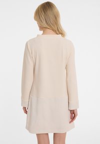Beiges Kleid mit langen Ärmeln, glatter Obertextur und geripptem unteren Abschnitt. Verfügt über einen runden Ausschnitt und umschlagbare Ärmel.