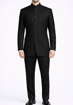 Homme portant un costume noir à col Nehru avec des boutons sur le devant, un pantalon noir et des chaussures habillées noires, debout devant un fond blanc.