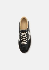 Mustad musta sneaker, mille pealisosa on valmistatud nahast ja seemisnahast, kreemjad paelad ja valged külgroosid. Pehme beež sisemus ja pruun põhi. Kaubamärgi logo on nähtav.