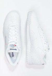 Chaussures de sport blanches en cuir avec une texture lisse. Elles présentent des coutures ton sur ton, un bout perforé et une fermeture à lacets. Détail du logo sur le talon.