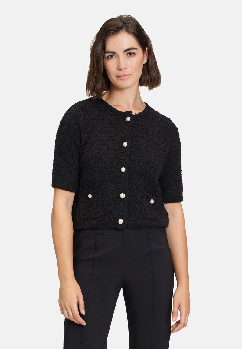Schwarze Kurzarm-Cardigan mit strukturierter Oberfläche, rundem Ausschnitt und vorderem Knopfverschluss; verfügt über zwei Taschen mit dekorativen Knöpfen.