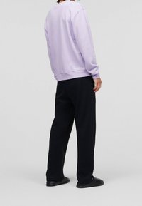 Lila sweatshirt met ronde hals en ribgebreide zoom, gecombineerd met zwarte wijd-uitlopende pantalon en zwarte instappers, van achter bekeken.