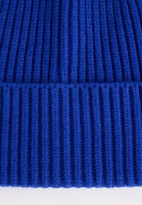 Raittupäinen sininen pipo, joka on valmistettu pehmeästä neulemateriaalista. Sen ominaisuuksiin kuuluu teksturoitu kuvio, jossa on voimakkaat pystysuorat urat, tarjoten joustavuutta ja lämpöä.