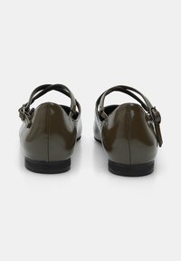 Zapatos de charol marrón con un diseño de punta redondeada, correa trasera y cierre de hebilla, que cuentan con un tacón negro bajo.