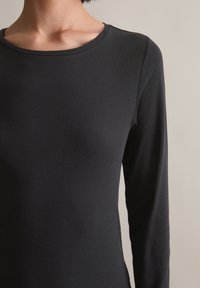 Langärmliges schwarzes Oberteil aus gerippter Textur mit einem weiten, runden Ausschnitt. Der Stoff wirkt leicht und glatt und schmiegt sich eng an den Körper.