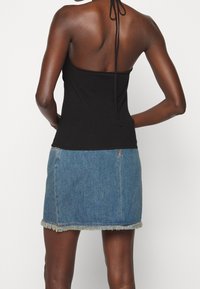 Haut noir à col licou avec dos ouvert, associé à une mini-jupe en denim bleu clair avec un ourlet effiloché et une fermeture éclair.