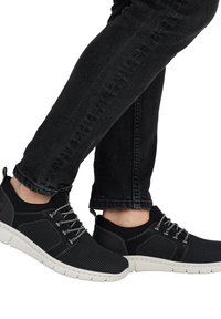 Czarne sneakersy z fakturowaną cholewką, elastycznymi sznurówkami i białymi podeszwami. Połączone z ciemnymi denimowymi spodniami o dopasowanym kroju.