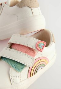 Hvide lædersneakers med velcrostropper, der har et flerfarvet filt regnbue-design og en lys beige ruskinds hæl accent.