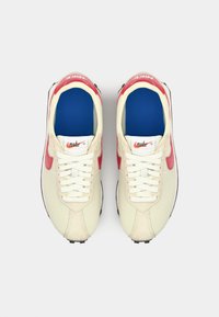 Beige mesh sneakers with red accents and white laces. Features a blue insole and textured rubber outsole. Nike branding on the tongue.
