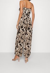 Mono negro con estampado de hojas beige, que presenta un top ajustado, un diseño de pernera amplia y tirantes ajustables. Combinado con sandalias de tacón a juego.