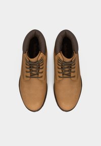 Ζευγάρι ταμπά δερμάτινων μποτών με κορδόνια και επενδυμένους σκούρους καφέ γιακάδες, σε θέα από πάνω σε λευκό φόντο.