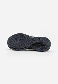 Semelle en caoutchouc noir d'une basket avec des motifs de bande de roulement texturés et un coussin d'air visible près du talon sur fond blanc.