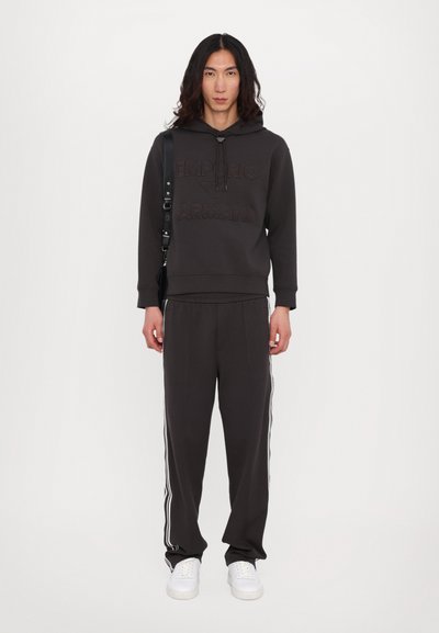 Hoodie cinza escuro com logótipo em relevo, calças de fato combinando com riscas brancas laterais e sapatilhas brancas. Textura suave e corte descontraído.