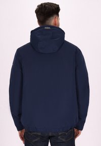 Giacca con cappuccio di colore blu navy, realizzata in un tessuto leggero e liscio. Presenta polsini elasticizzati e orlo aderente, senza loghi visibili sul retro.