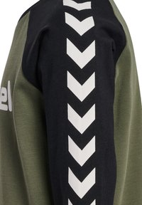 Grön och svart sweatshirt med vitt sicksackmönster längs ärmarna. Tillverkad av mjukt material, med rund halsringning och avslappnad passform.