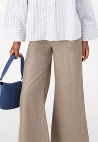 Light blue and white striped button-up shirt with wide cuffs, paired with beige wide-leg trousers. A small blue bag is held by the hand.