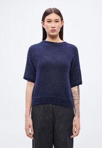 Μπλε σκούρο πλεκτό πουλόβερ με κοντά μανίκια, στρογγυλή λαιμόκοψη και ριμπ τελείωμα. Μαλακή υφή, σε συνδυασμό με παντελόνι φαρδύ σε σκούρο γκρι χρώμα.