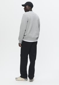 Gray sweatshirt with ribbed cuffs, paired with black pants and gray sneakers. The model wears a black cap, facing away from the camera.