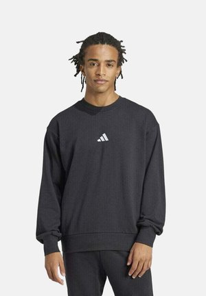 Felpa nera realizzata in tessuto morbido, con colletto a girocollo e polsini a costine. Un piccolo logo Adidas bianco è centrato sul petto.