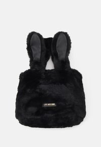 Černá kabelka z umělé kožešiny s dlouhýma zajíčíma ouškama, zdobená koženým detailem a zlatou značkovou visačkou. Měkká textura a zaoblený tvar.