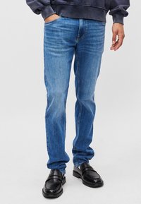 Jeans din denim albastru cu picioare drepte, cu un aspect diluat, manșete pentru curea, buzunare laterale și o textură rezistentă, asortați cu mocasini din piele neagră.