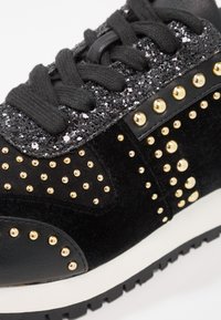 Baskets noires avec tissu pailleté près des lacets, lacets noirs et clous ronds dorés sur panneaux en velours noir et cuir.