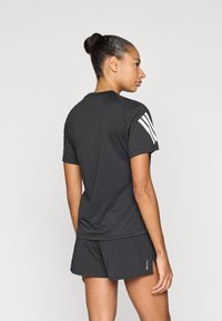 Czarny sportowy T-shirt z krótkim rękawem, z białymi paskami na ramieniu, w komplecie z dopasowanymi szortami. Gładka faktura, luźny krój.