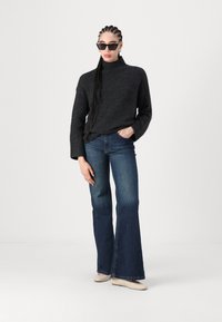 Pulover turtleneck gri închis, cu croi lejer, asortat cu blugi evazați bleu deschis și balerini bej. Accesoriile includ ochelari de soare negri și cercei rotunzi.