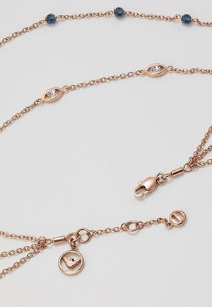 Náhrdelník ve vrstveném designu z růžového zlata s modrými korálky, průhlednými krystalovými články ve tvaru oka, karabinkou a kulatým přívěskem značky na světlém pozadí.
