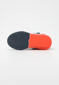 Sko soles har en svart teksturert gummiseksjon med røde detaljer. Designet inkluderer mønstrede spor for grep og stabilitet.