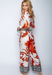 Dwuczęściowy strój w kwiatowy wzór, składający się z bluzki z krótkim rękawem i spodni o szerokich nogawkach. Biała tkanina z wyrazistymi pomarańczowymi kwiatami i czarną lamówką.