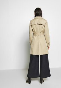 Trinchado beige con cintura ceñida, frente de doble botonadura y epauletes en los hombros. Combinado con pantalones de mezclilla oscuros de pierna ancha y botas hasta el tobillo.