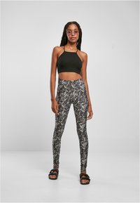 Crni halter crop top uparen s tajicama visokog struka koje imaju bijeli apstraktni uzorak. Model nosi crne sandale; pozadina je neutralna.