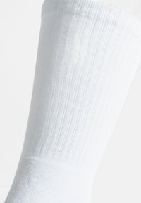 Calcetín blanco de canalé hasta la rodilla, hecho de un material suave y elástico con una textura suave y un puño reforzado para mayor durabilidad.