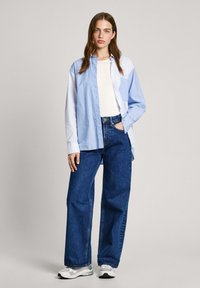 Overhemd met een blauw-wit gestreept patroon, gecombineerd met losse blauwe jeans en witte sneakers. Gladde stof, casual pasvorm.