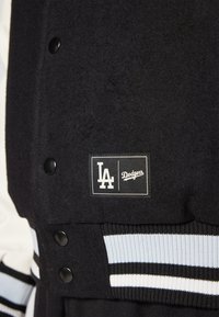 Svart ullblandings varsity-jakke med trykknapper, stripete ribbede mansjetter i lyseblått og svart, med Dodgers-logo på merket.